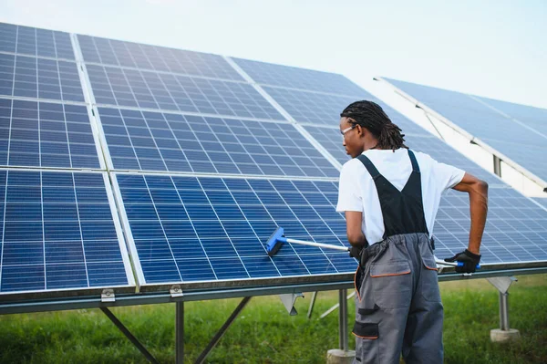 Afro-Amerikan işçiler bir açık hava fotovoltaik güç istasyonunda güneş panellerini temizliyor.