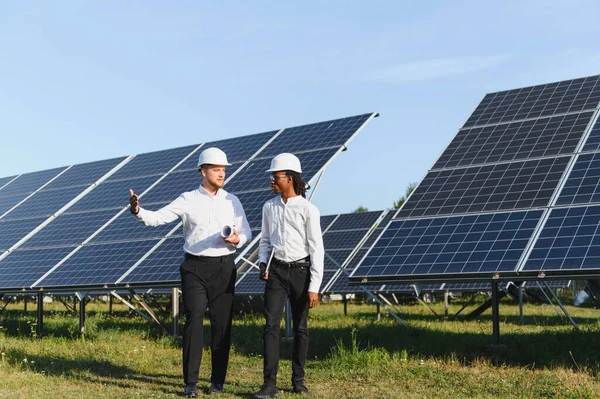 Güneş paneli alanında yürüyen iki mühendis yenilenebilir enerji ve sürdürülebilirliği tartışıyor.