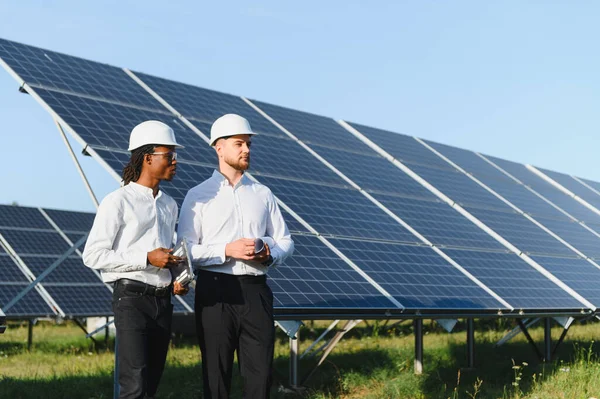 Güneş paneli alanında duran iki farklı mühendis yenilenebilir enerji ve sürdürülebilirlik çözümlerini tartışıyor.