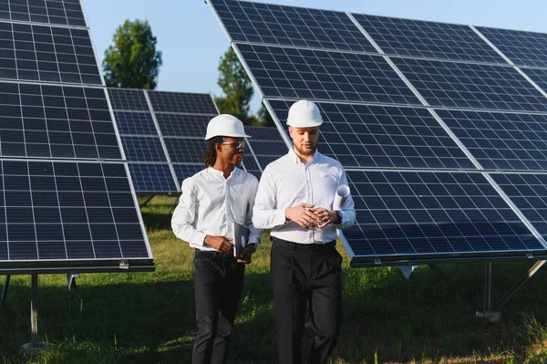 Büyük bir güneş çiftliğinde yürüyen mühendislerden oluşan çeşitlilik ekibi yenilenebilir enerji projesinin uygulanması ve sürdürülebilirliğini tartışıyor.