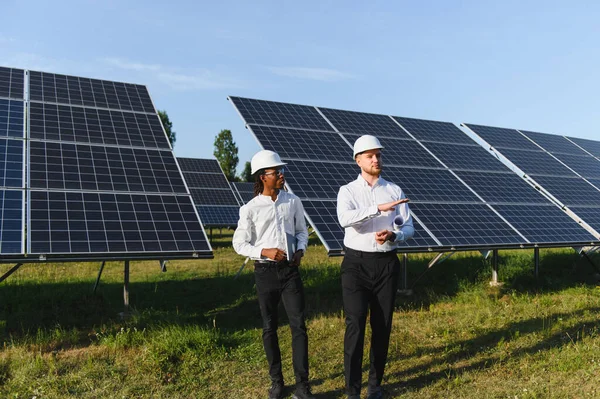 İki farklı mühendis bir güneş enerjisi santralinde operasyonları tartışıyor, takım çalışması ve sürdürülebilir enerji gelişimi.