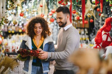 Mutlu çift Noel çelengini seçerken gülümsüyor. Tatil alışverişi sırasında rahat, süslü bir mağazada.