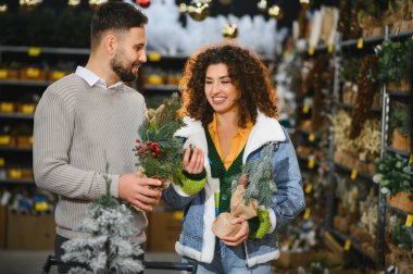 Mutlu çift bir mağazada birlikte Noel süslemeleri seçiyor. Tatil evi dekorasyonu ve hediyeler için alışveriş yaparken gülümsüyorlar.