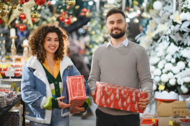 Mutlu çift perakende mağazasında bayram hediyeleri alıyor, neşeli tatil sezonunu kutluyorlar, hediyeler alıyorlar.
