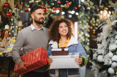 Mutlu çift ellerinde hediyeler, ağaçlar ve ışıklarla süslenmiş bayram alışverişi yapıyorlar.