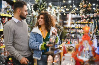Bir tatil mağazasında Noel süsleri ve süslerine bakan genç bir çift festival sezonu için eşyalar seçiyor.