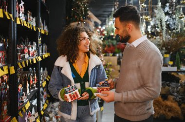 Genç mutlu çift perakende mağazasında Noel süsleri seçiyor, birlikte kış tatili alışverişinin keyfini çıkarıyorlar.