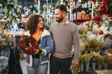 Mutlu çift bir mağaza koridorunda yürürken bayram çelengi seçiyor, kış kutlamalarına hazırlanıyor.