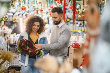 Mutlu çift Noel çelengini süslerle ve kozalaklarla süslenmiş bir bayram mağazasında seçiyor.