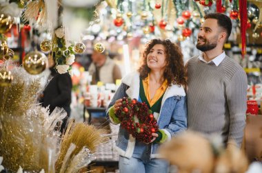 Mutlu çift bayram süslemelerini seçiyor, Noel pazarının ve mevsimlik alışveriş faaliyetlerinin tadını çıkarıyor.