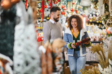 Mutlu çift, bayram süsleri ve mevsimlik dekorlar seçiyor, gülümsüyor ve kış tatili için neşeli bir alışveriş deneyimi paylaşıyor.