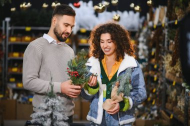 Genç çift tatil süslemeleri seçiyor, küçük bir Noel ağacı seçiyor ve mevsimlik bir mağazada kış alışverişinin tadını çıkarıyor.