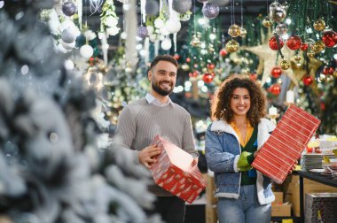 Gülümseyen bir çift ellerinde paketlenmiş hediyeler, bayram mağazasından hediye ve dekorasyon alışverişi yapıyorlar.