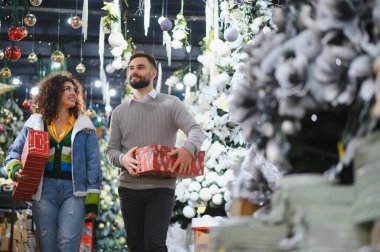 Mutlu çift bir festival mağazasında yürüyor, ellerinde hediyeler, bayram hediyeleri ve dekorasyonlar var.