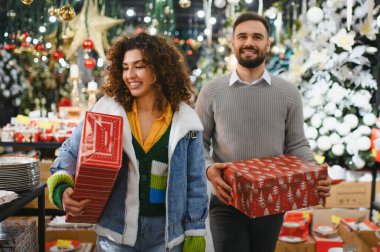 Gülümseyen bir çift bir mağazada hediye paketliyor, neşeli atmosferin tadını çıkarıyor ve Noel için hazırlanıyor.