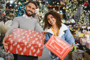 Mutlu genç çift, süslü bir mağazada gülümsüyor, Noel hediyelerini paketleyip birlikte alışverişe çıkıyorlar.