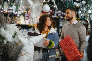 Birbirlerine bakan genç çift, hediye ve dekorasyonlarla bayram alışverişi yapıyorlar.