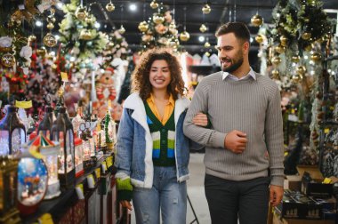 Bir çift bayram mağazasında yürüyor, noel süsleri alıyor ve tatil sezonunu birlikte kutluyorlar.