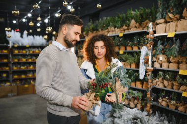 Bayram mevsimi için Noel süsleri seçen çiftler, küçük yapay ağaçlar ve şenlikli dallar arasında seçim yapıyorlar.