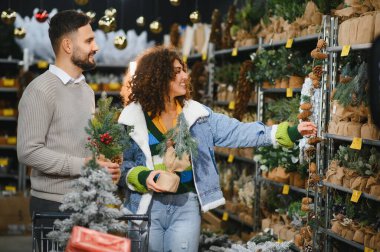 Mutlu çift, bayram süslemelerini ve perakende mağazasında suni Noel ağaçlarını seçiyor. Kış kutlaması için hazırlanıyorlar.