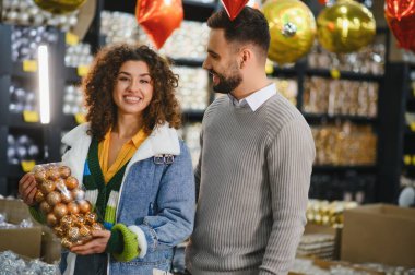Genç çift mağazalardan Noel süsleri seçiyor, gülümsüyor ve bayram alışverişinin tadını çıkarıyor, mevsimsel neşe