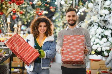 Genç, gülümseyen bir çift ellerinde hediyelerle bayram alışverişinin keyfini çıkarıyorlar.
