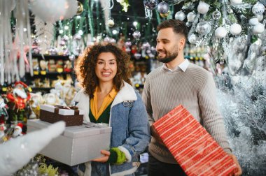 Mutlu çift mağazada hediyeler ve dekorasyonlar seçiyor, birlikte bayram alışverişinin tadını çıkarıyor, gülümsüyor.
