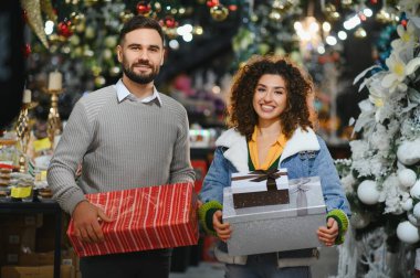 Genç çift hediyelerini paketliyor, gülümsüyor Noel için süslenmiş bir bayram mağazasında hediye alırken.