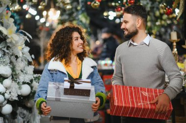 Genç çift gülümsüyor ve paketlenmiş hediyeler taşıyor, bayram mevsimini kutluyor ve tatil alışverişi yaparken aşkı paylaşıyor