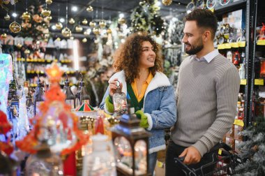 Gülümseyen genç çift, tatil sezonu için parlak bir perakende mağazasında şenlik dekorasyonları seçiyor.
