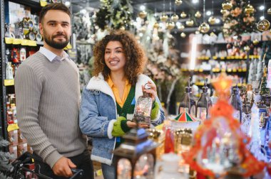 Mutlu çift bir perakende mağazasında dekoratif eşyalar ve kar küreleri seçiyor, Noel tatili sezonuna hazırlanıyorlar.