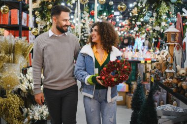 Bir çift mağaza koridorunda yürüyor, Noel süslemeleri seçiyor ve birlikte bayram alışverişinin tadını çıkarıyor.