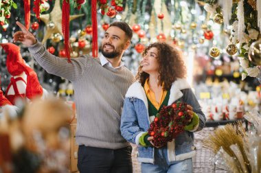 Şenlikli süsleri ve tatil çelenklerini seçen mutlu genç çift, kış kutlaması için hazırlanıyor.