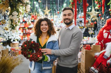 Gülümseyen çift parlak bir mağazada her daim yeşil bir çelenk seçiyor, bayram süsleri hazırlıyor ve birlikte neşe paylaşıyorlar.