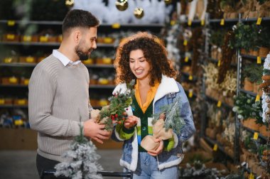 Perakende mağazasında bayram dekorasyonlarını karşılaştıran genç çift, yaklaşan kış mevsimi kutlamalarına hazırlanıyor.