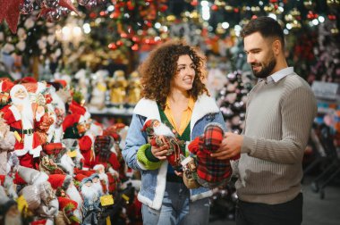 Mutlu çift Noel Baba figürleri ve bayram süsleri satan bir mağazadan şenlikli süsler seçiyor.