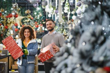 Mutlu çift, hediye paketlerini tutarken gülümsüyor, gelecek tatil sezonu için süslemeler ve hediyeler alıyor.