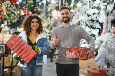 Genç çift gülümsüyor, hediye paketliyor ve bayram alışverişinin tadını çıkarıyor.