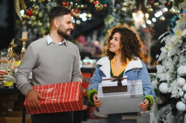 Noel alışverişinde hediye kutuları taşıyan ve birbirlerine gülümseyen mutlu bir çift.