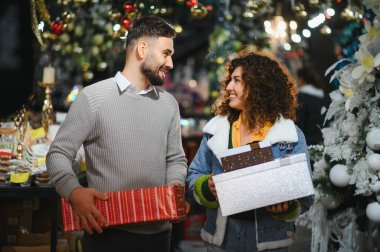 Mutlu genç çift gülümsüyor, hediye paketliyor ve bayram alışverişinin tadını çıkarıyor.