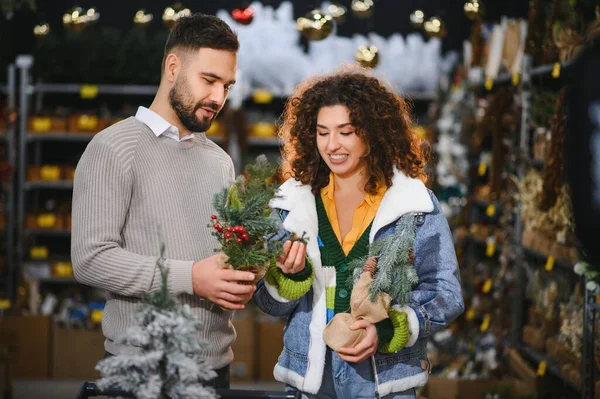 Genç çift tatil süslemeleri seçiyor, küçük bir Noel ağacı seçiyor ve mevsimlik bir mağazada kış alışverişinin tadını çıkarıyor.