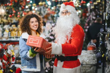 Noel Baba, bayram alışverişini kutlayan ve hediye veren gülümseyen bir kadınla hediye paylaşıyor.