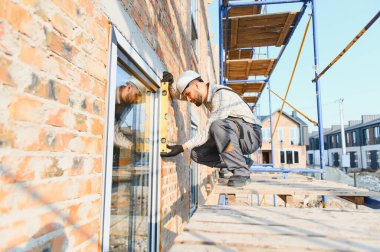 İnşaatçı, yeni bir konut projesinde tuğla bir duvarda ruh seviyesini kullanarak pencere çerçevesi kuruyor