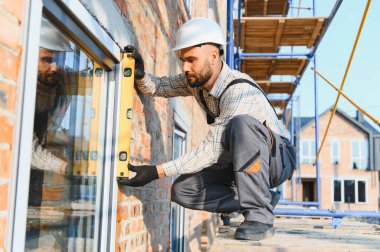 İnşaat işçisi iskele üzerinde dururken pencere seviyesini kontrol ediyor. Yeni ev inşa ediliyor