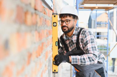 Duvarda ruh seviyesini kullanan genç bir adam inşaat sırasında hassasiyet ve kaliteyi sağlıyor.