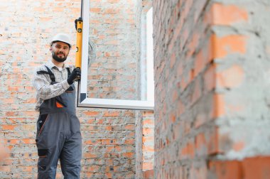 İnşaat alanındaki yeni pencere çerçevesini kontrol eden profesyonel işçiler, ev geliştirme ve inşaat çalışmalarına odaklanıyor