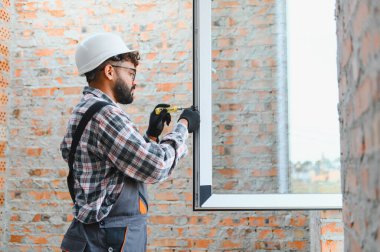 Pencere kurulumunu tamamlayan inşaat işçisi, yeni binadaki ayarları ayarlamak için tornavida kullanıyor