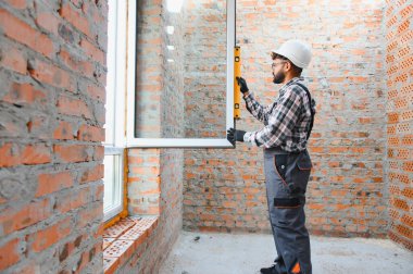 Erkek inşaat işçisi binaya yeni pencere kuruyor, ruhsal seviyeyle dikey hizayı kontrol ediyor, başlık takıyor