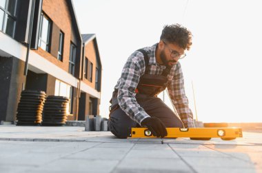 Yeni inşaat alanında çalışan genç bir adam, teras geçitleri kuruyor ve ruh seviyesini kullanarak düz bir yüzey sağlıyor.