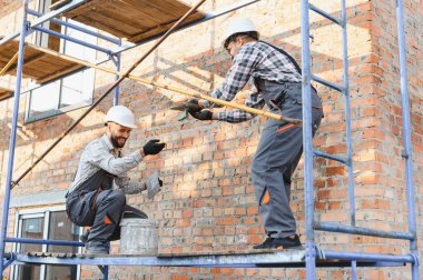 Tuğla ustalarından oluşan bir ekip bina duvarı inşa ediyor. Yeni ev inşaatında birlikte çalışan profesyonel müteahhitler.